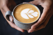 A woman holding a barista-made coffee that has a leaf design in the milk froth.